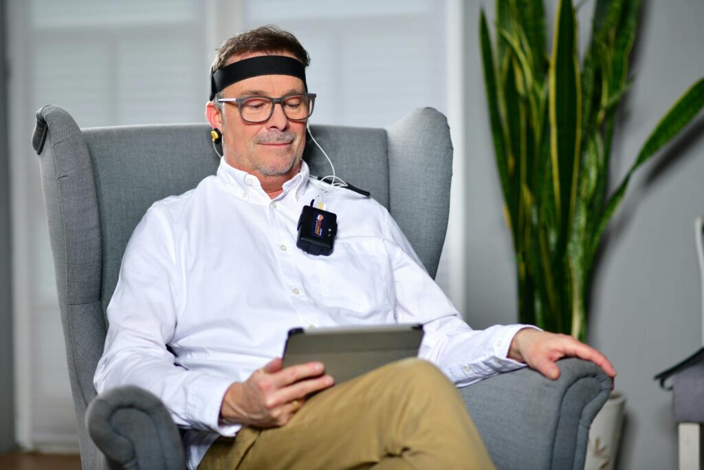 Man sitting in an armchair using a neurofeedback device, illustrating modern technology in healthcare.